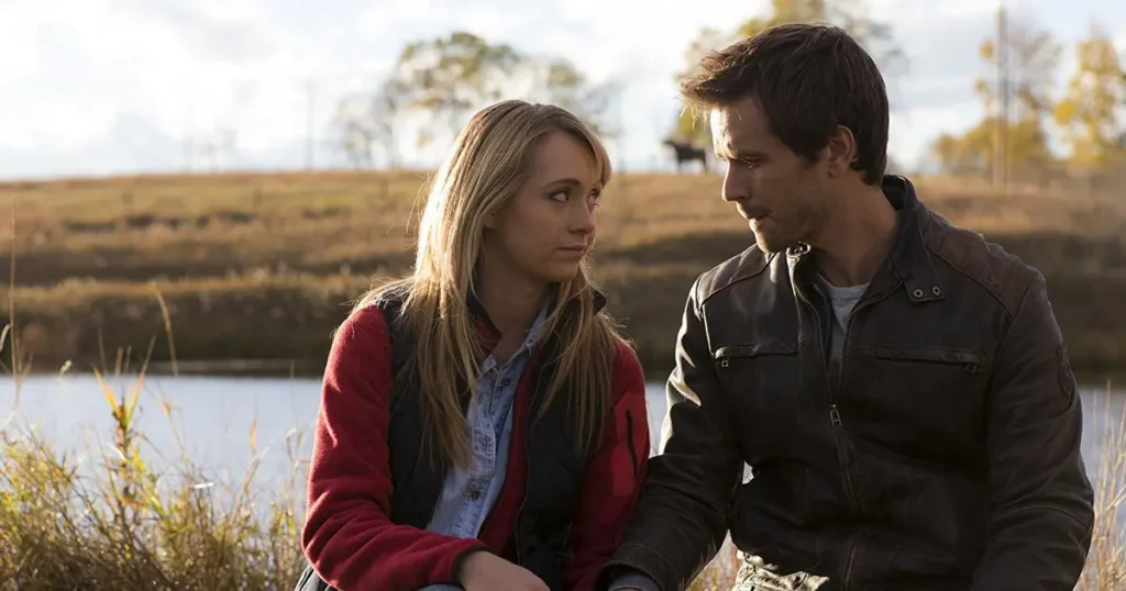 Amy Fleming and Ty Borden sitting together by a lake on Heartland, holding hands and looking at each other