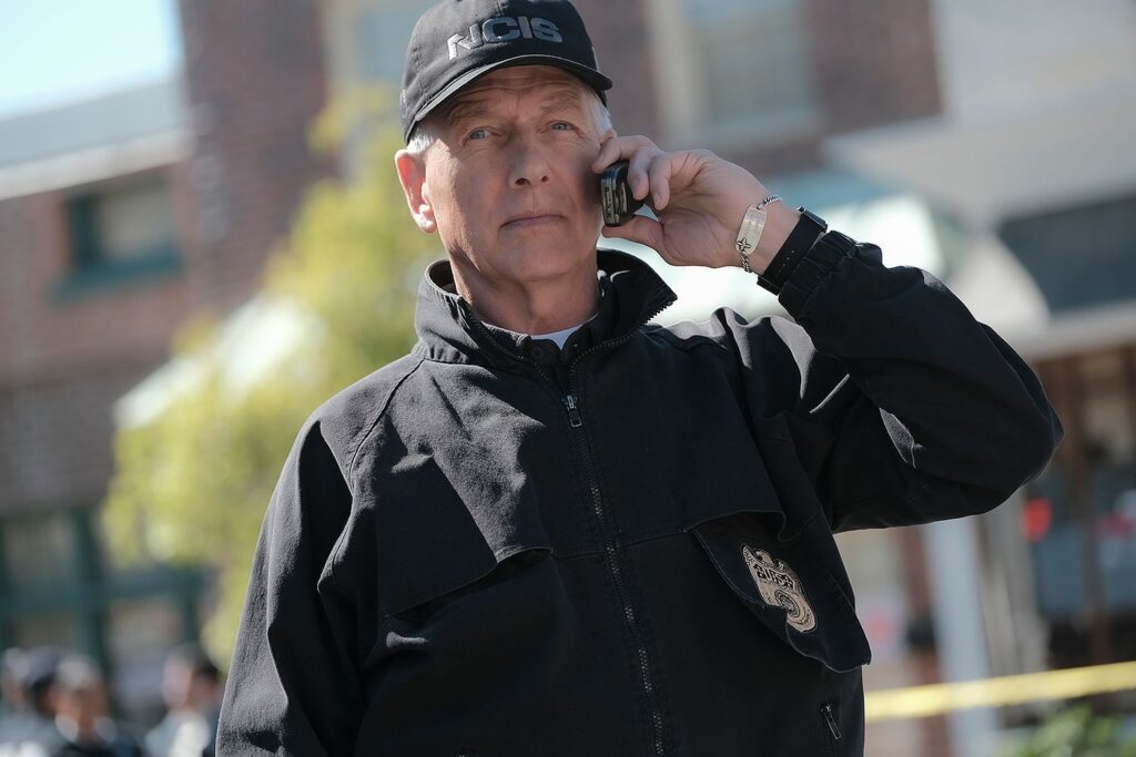 Mark Harmon as Gibbs in an NCIS cap, on the phone at a crime scene
