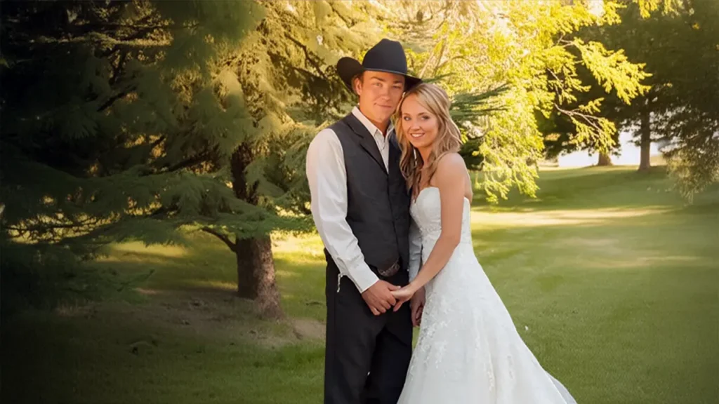 Amber Marshall in a white wedding dress holding hands with her groom, Shawn Turner, in cowboy attire, standing outdoors on their wedding day.