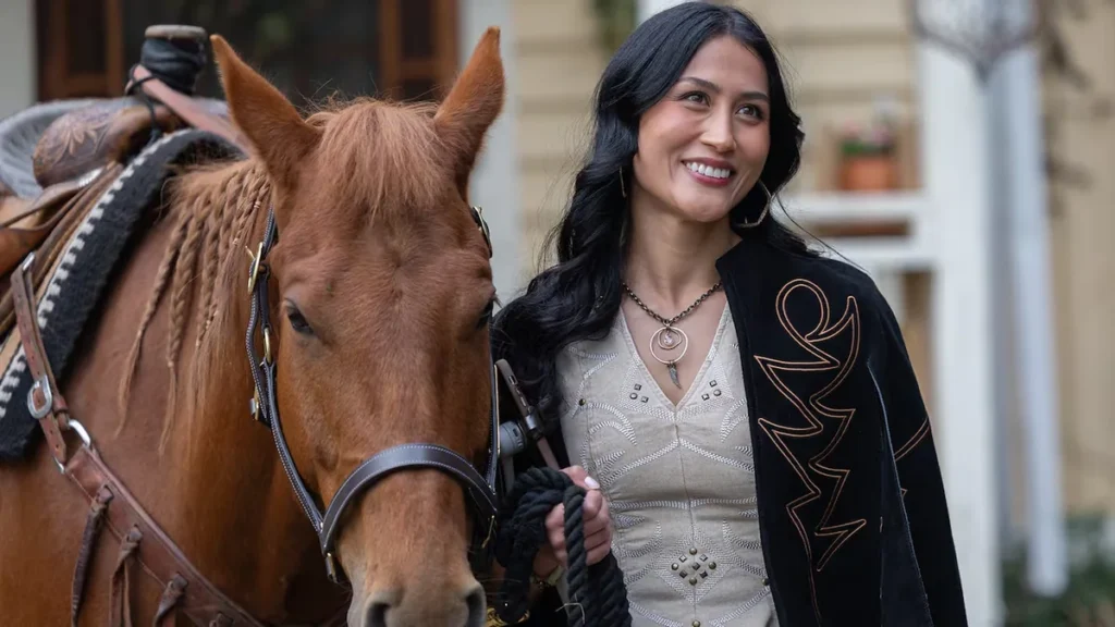 Brynn Godenir as Winn Becker smiling beside a saddled chestnut horse with a braided mane on Heartland Season 20